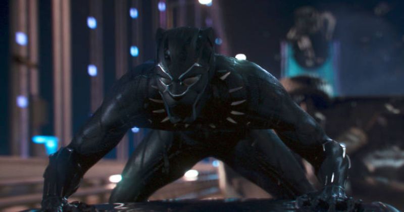 Black Panther ในชุดสีดำเงาที่เป็นเอกลักษณ์ กำลังหมอบอยู่บนหลังคารถยนต์ ท่าทางของเขาบ่งบอกถึงความพร้อมในการต่อสู้ ฉากหลังเป็นเมืองในยามค่ำคืน จากเรื่อง Black Panther 2018