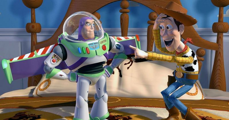 วู้ดดี้ คาวบอยตุ๊กตา ยิ้มและชี้นิ้วไปที่บัซ ไลท์เยียร์ นักบินอวกาศตุ๊กตา ซึ่งมีสีหน้าจริงจังและสับสนเล็กน้อย ทั้งคู่อยู่ในห้องนอนของเด็กชาย โดยมีเตียงไม้เป็นฉากหลัง จากเรื่อง Toy Story ทอย สตอรี่